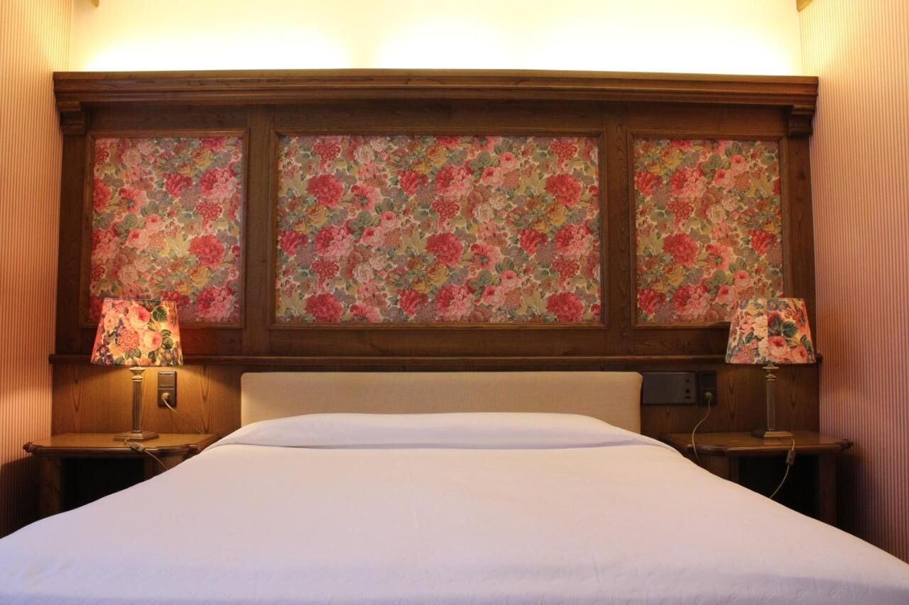 Camera d'albergo con un letto grande, due comodini e una testiera decorata con motivi floreali.