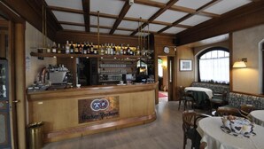 A bar area with a wooden counter, shelves of bottles, and a clock on the wall. There are tables and chairs in the dining area.
