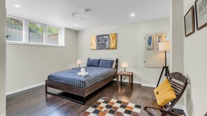 A bedroom with a bed, bedside tables, a chair, a lamp, and artwork on the walls. - Stylish Zen Stay Mins to Falls | BBQ Area (Niagara Falls)