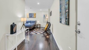 A hallway with a bed, a chair, a small table, and artwork on the walls. - Stylish Zen Stay Mins to Falls | BBQ Area (Niagara Falls)