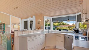 Eine moderne Küche mit einer großen Kochinsel, weißen Schränken und Blick auf den Garten durch das Fenster.