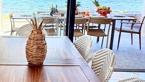 An outdoor dining area with a view of the ocean, featuring wooden tables and wicker chairs. - VIlla Opale — Luxury Living by the Sea (Oyster Pond)