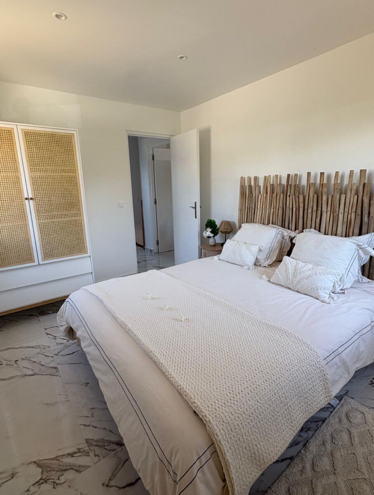 A bedroom with a large bed, a wooden headboard, a rattan wardrobe, and a view of a hallway.