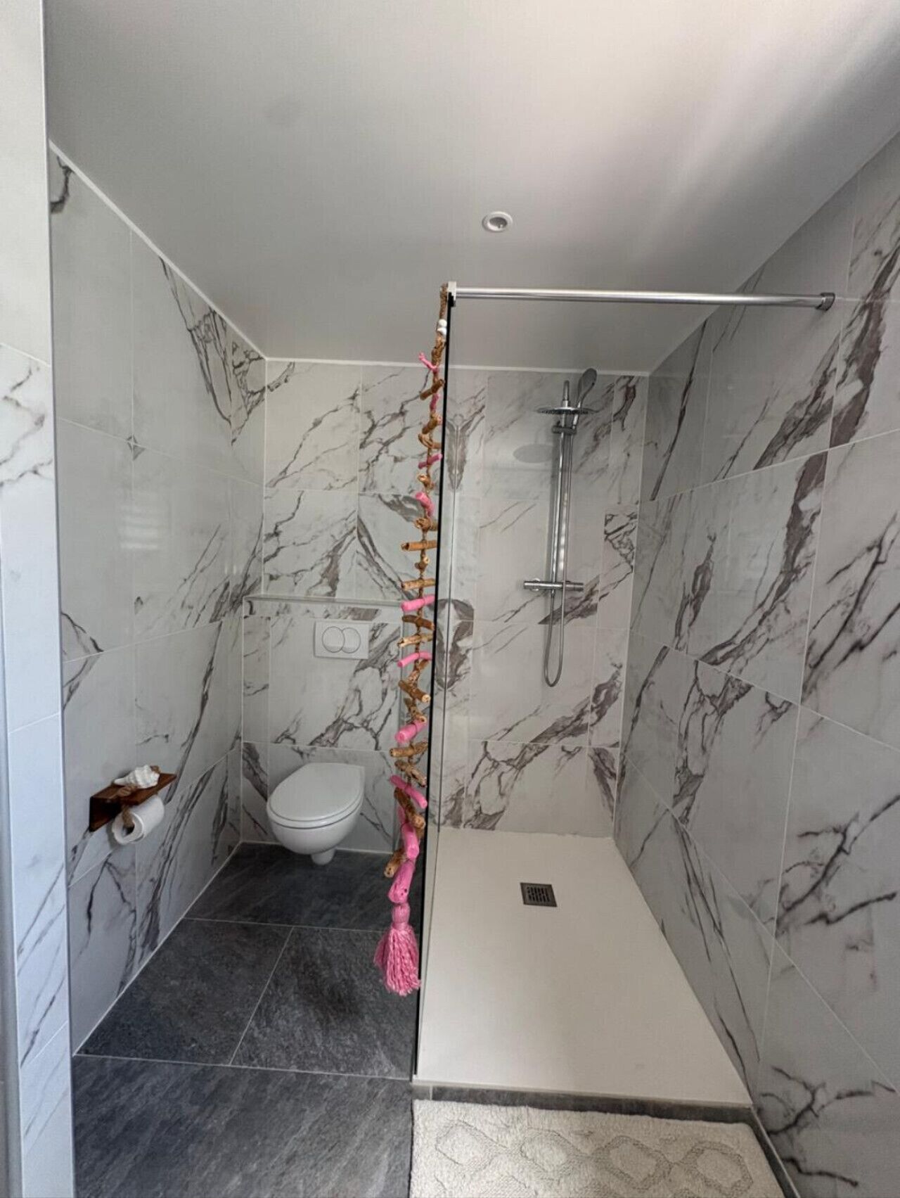 Une salle de bain moderne avec des murs en marbre, une douche en verre, des toilettes et un porte-serviettes.