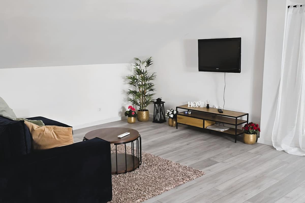 A modern living room with a sofa, a coffee table, a TV mounted on the wall, and a wooden TV stand with decorative items.