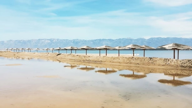A beach with rows of umbrellas and a calm sea, with mountains in the background. - Villa Casa Mia Sabunike (Privlaka)