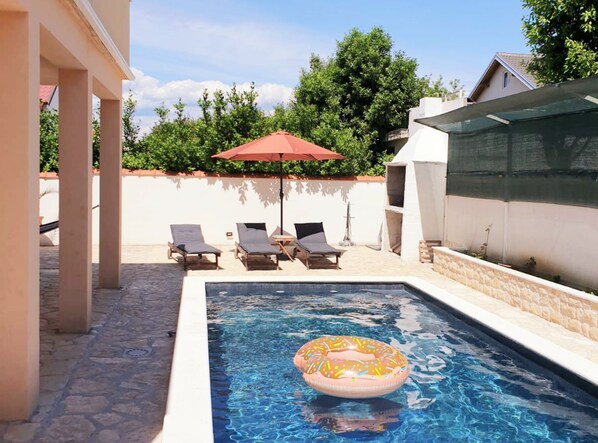 Piscina com espreguiçadeiras e um guarda-sol.