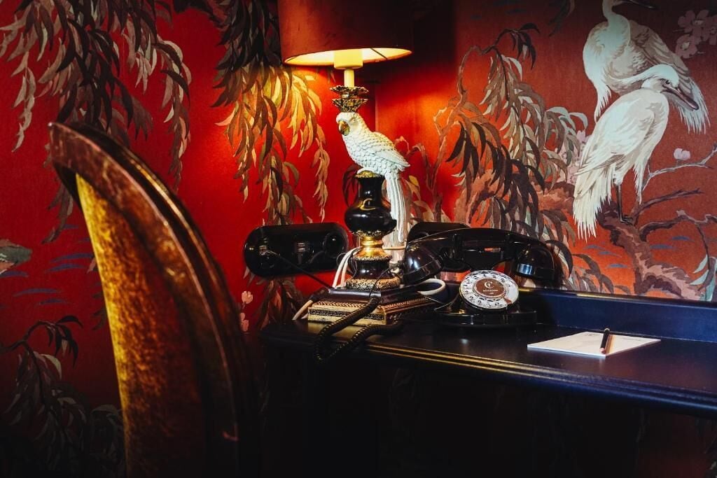 A room with a desk, a telephone, a lamp, and a wall with a bird mural.