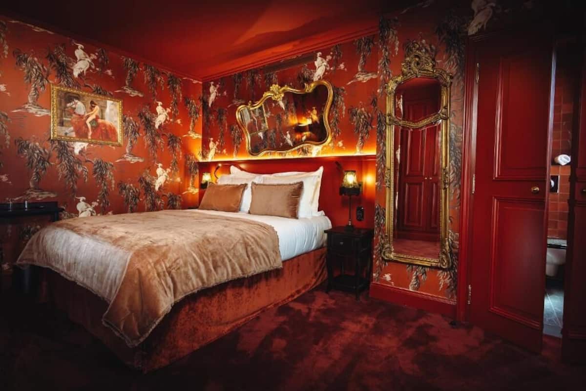 Une chambre dotée d’un grand lit, d’un miroir décoratif et de murs rouges ornés de motifs floraux.