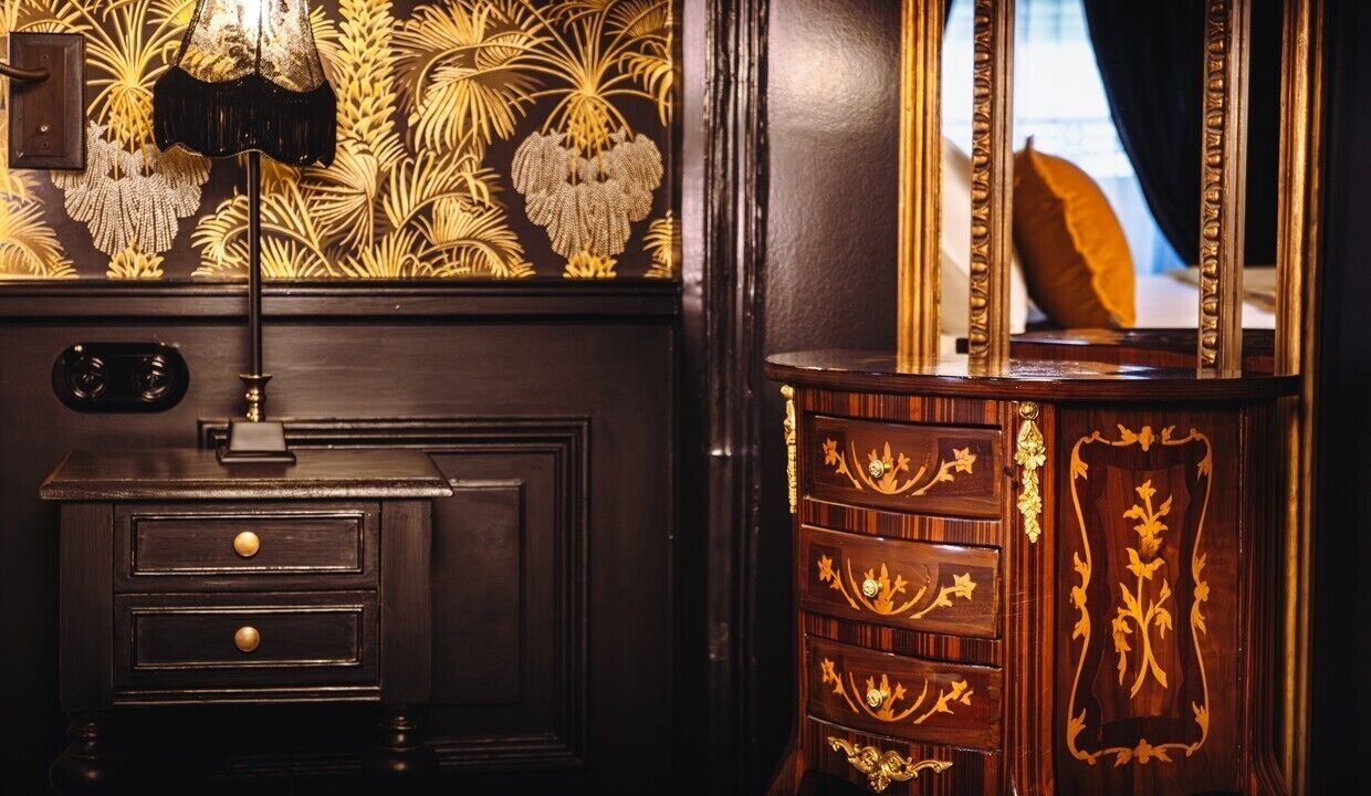 Een donkere houten dressoir met ingewikkelde gouden decoraties en een spiegel met gouden lijst.