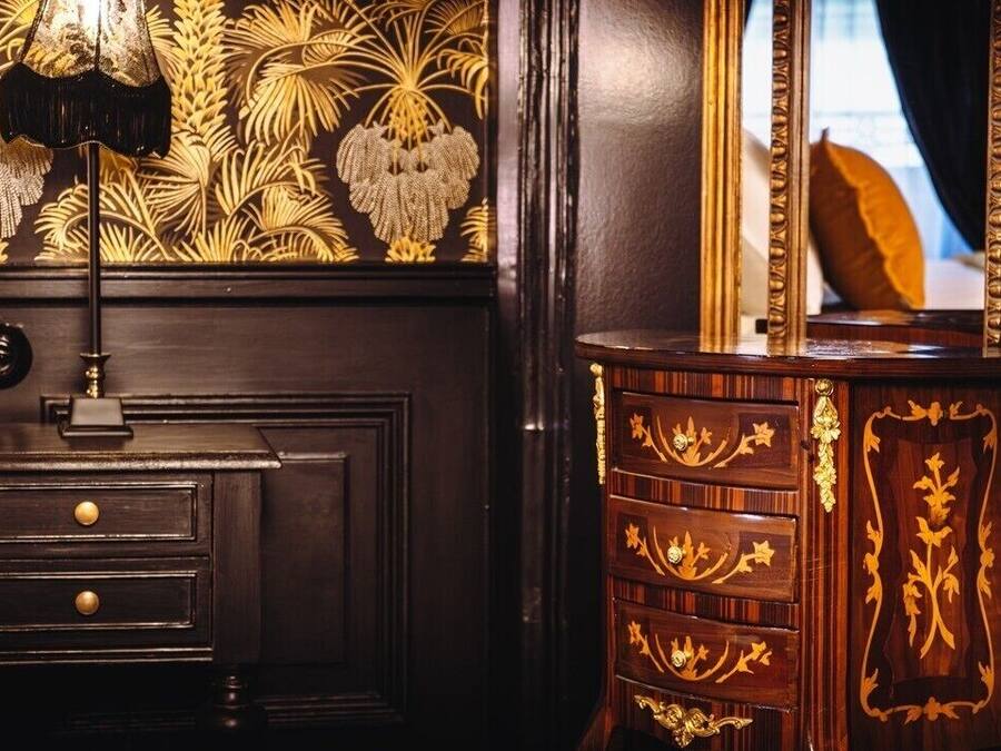 Een donkere houten dressoir met ingewikkelde gouden decoraties en een spiegel met gouden lijst.