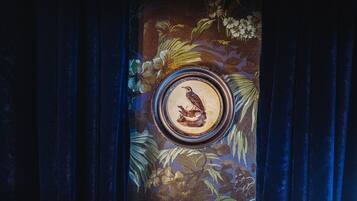 A framed artwork of a bird on a branch, surrounded by floral patterns.