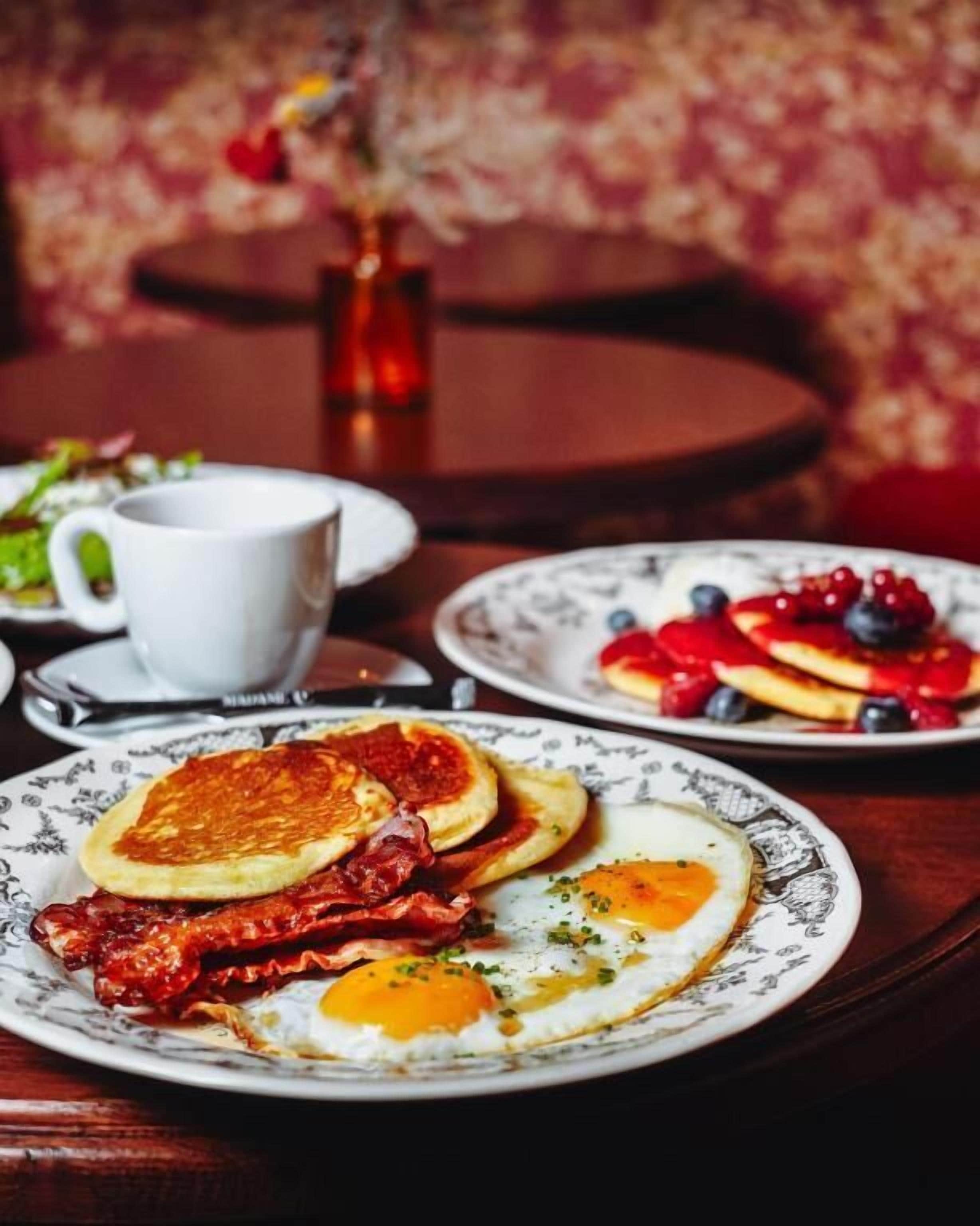 A breakfast setting with pancakes, eggs, and berries on plates, a cup, and a vase with flowers.