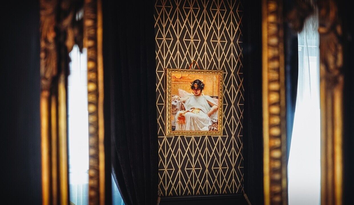 A framed portrait of a woman in a white dress against a geometric patterned wall.