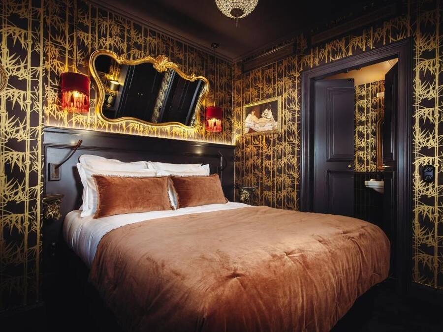A luxurious bedroom with a large bed, a mirror, and wall-mounted sconces.