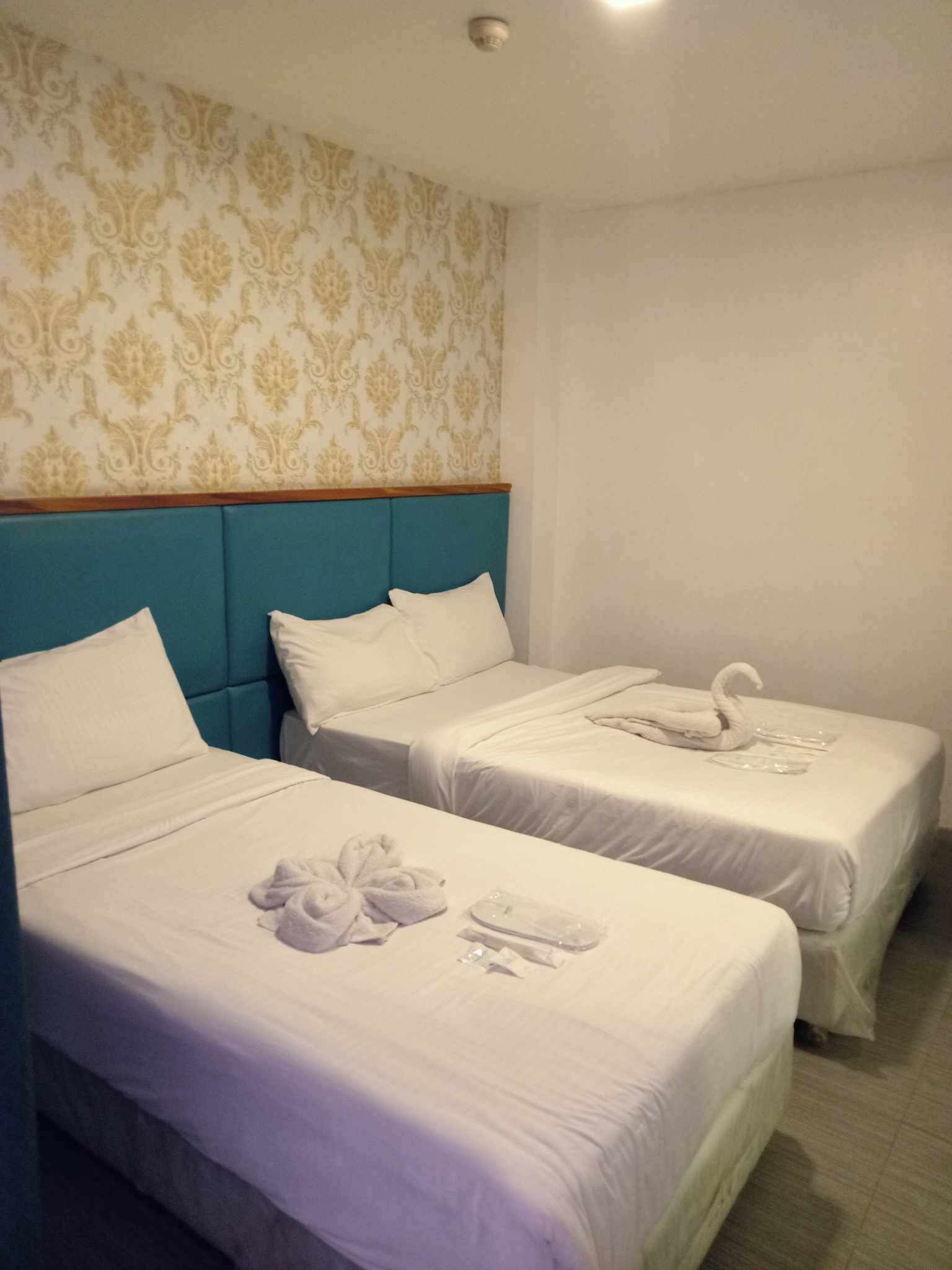 Ein Hotelzimmer mit zwei Betten, jeweils mit weißer Bettwäsche und einem blauen Kopfteil. Auf den Betten liegen Handtücher und ein zu einem Schwan geformtes Handtuch.