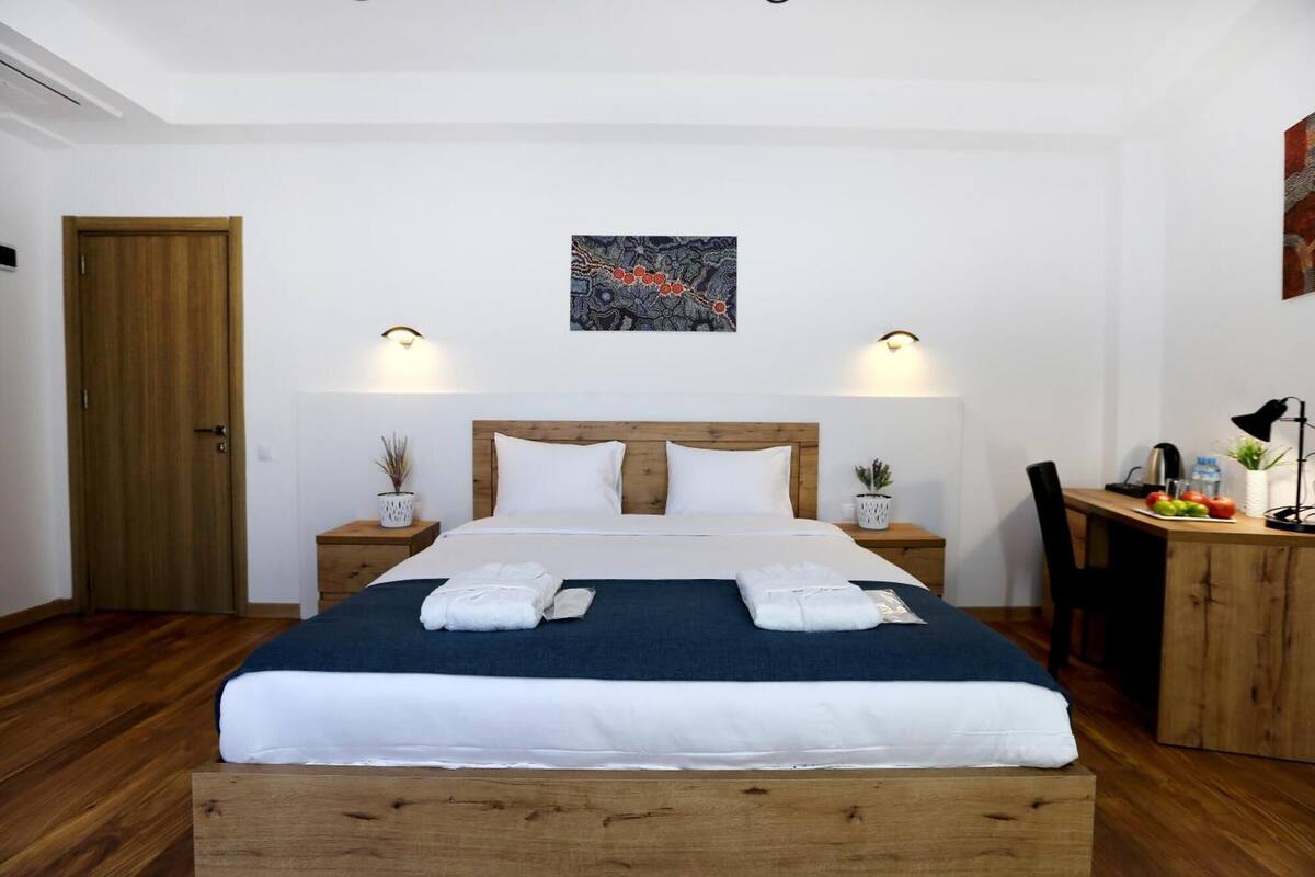 A neatly arranged hotel room with a wooden bed, white bedding, two bedside tables with lamps, a small desk with a chair, and a door.