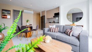 A modern living room with a grey sofa, wooden coffee table, and a dining area with a table and chairs.
