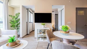 Una sala de estar moderna con un televisor de pantalla plana, asientos cómodos, una mesa de comedor y una planta en maceta.