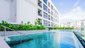 Un hotel moderno con piscina, rodeado de abundante vegetación y un edificio de varios pisos con balcones.