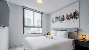 Ein modernes Hotelzimmer mit einem großen Bett, Blick auf die Stadt, einem Flachbildfernseher und einem minimalistischen Design.