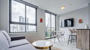Ein modernes Wohnzimmer mit einem grauen Sofa, einem runden Couchtisch und einem an der Wand befestigten Fernseher.