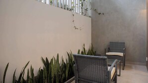 A modern outdoor seating area with wicker chairs and tall green plants.