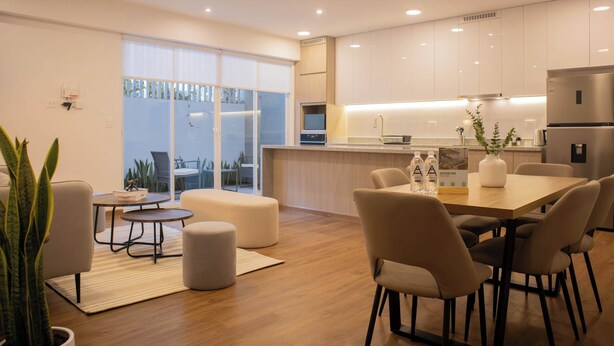 A modern kitchen with a central island, a dining area with a table and chairs, and a large sliding glass door leading to a balcony.