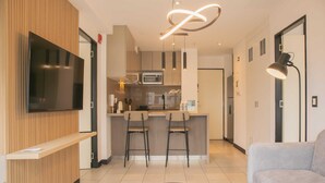 A modern living room with a flat-screen TV, a grey sofa, and a kitchen area with a microwave and bar stools. - w* | Incredible 2BR with Balcony in San Isidro (San Isidro)
