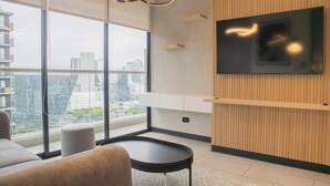 A modern living room with a large window, a flat-screen TV mounted on a wooden wall, and a round table. - w* | Incredible 2BR with Balcony in San Isidro (San Isidro)
