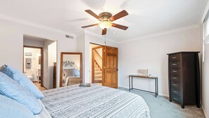 A bedroom with a bed, a ceiling fan, a dresser, and a small table.