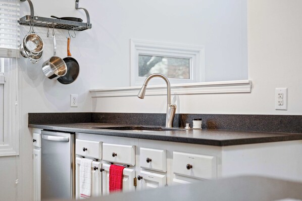 A kitchen with white cabinets, a stainless steel dishwasher, a black countertop, and a window above the sink. - Mass Ave Gem and steps away from Yoga Studio (Indianapolis)