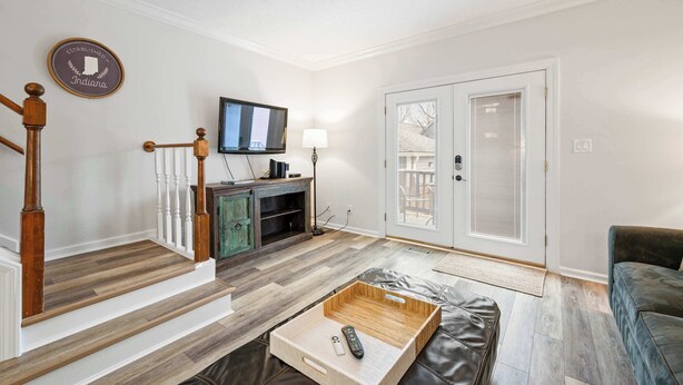 A living room with a wooden staircase, a flat-screen TV, a lamp, and a door leading outside.