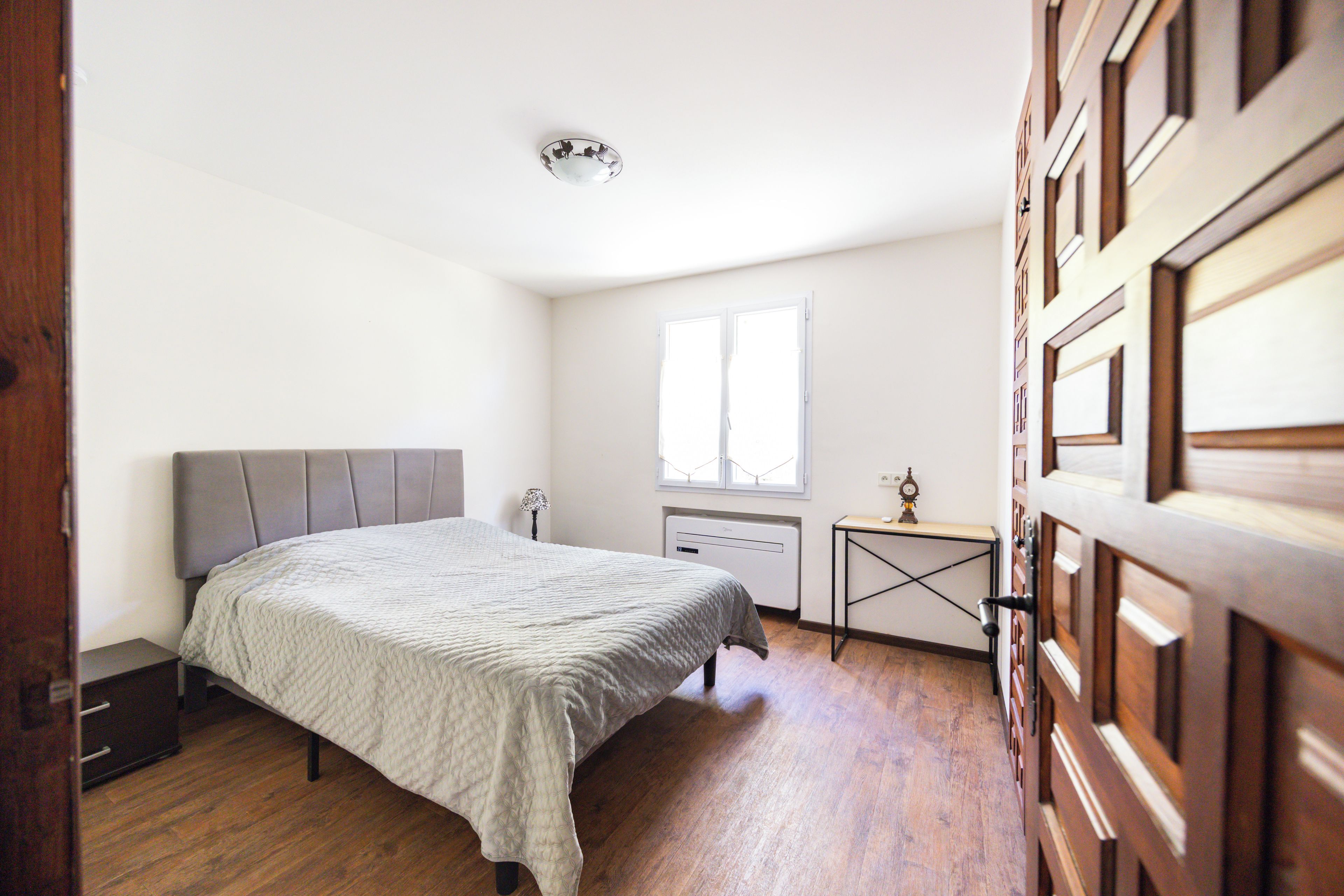 A bedroom with a bed, a bedside table, a lamp, a radiator, and a window.