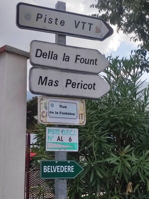 A directional signpost with multiple directions including 'Piste VTT,' 'Della la Fount,' 'Mas Pericot,' and 'Belvedere.'