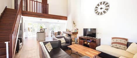 A spacious living room with a staircase, leather sofas, a wooden coffee table, and a large wall clock.