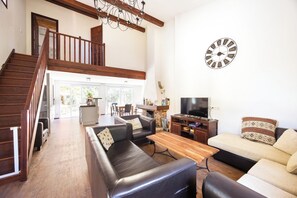 A spacious living room with a staircase, leather sofas, a wooden coffee table, and a large wall clock.