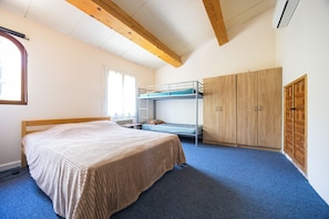 A room with a bunk bed, a single bed, a wardrobe, and a window.