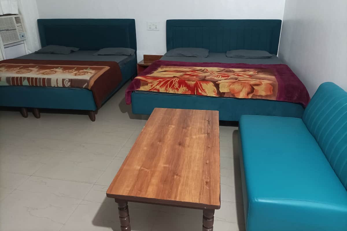 A room with two beds, a wooden table, and a teal sofa.