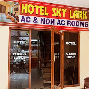 Un hotel llamado 'Hotel Sky Lark' con un letrero que indica 'Habitaciones con y sin aire acondicionado' y 'Servicio 24 Horas'.