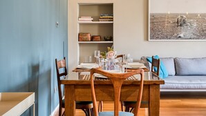 A dining area with a wooden table set for four, a bookshelf with books and decorative items, and a grey sofa in the background. - Easylife - Contemporary design in Porta Sempione (Milano)