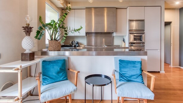 A modern kitchen with stainless steel appliances, a central island, and two chairs with blue cushions. - Easylife - Contemporary design in Porta Sempione (Milano)