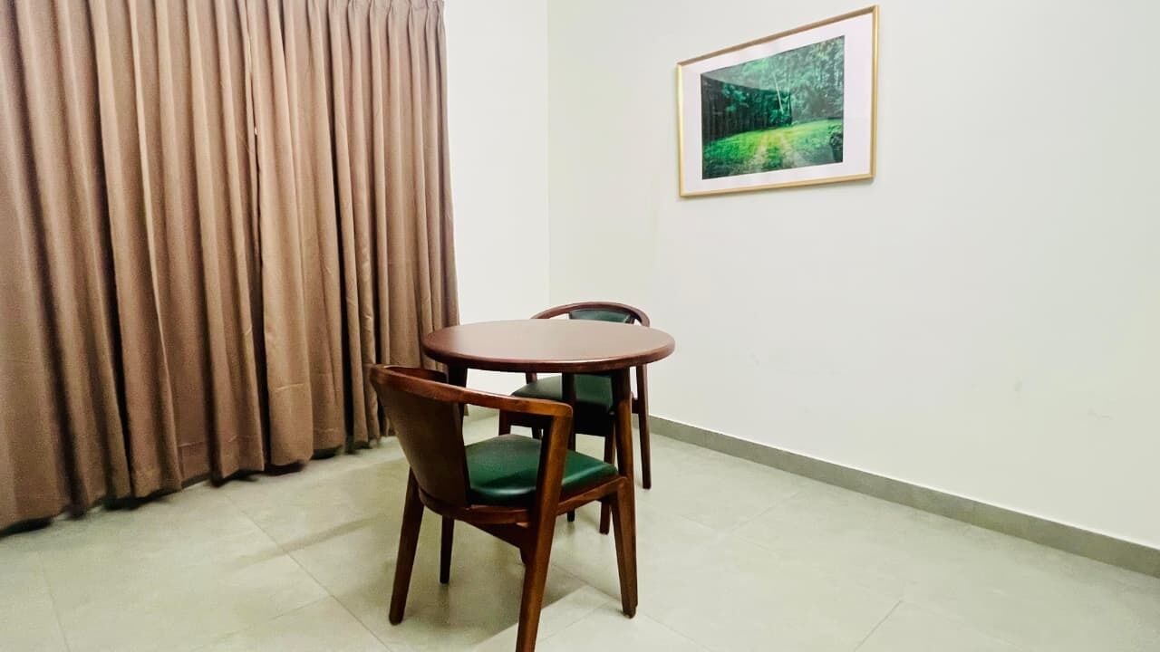 Ein Zimmer mit einem runden Holztisch, zwei Stühlen, einem gerahmten Bild an der Wand und einem Vorhang am Fenster.