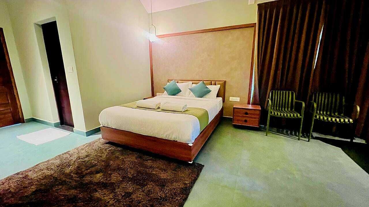 A bedroom with a bed, a nightstand, a chair, and a large window with curtains.