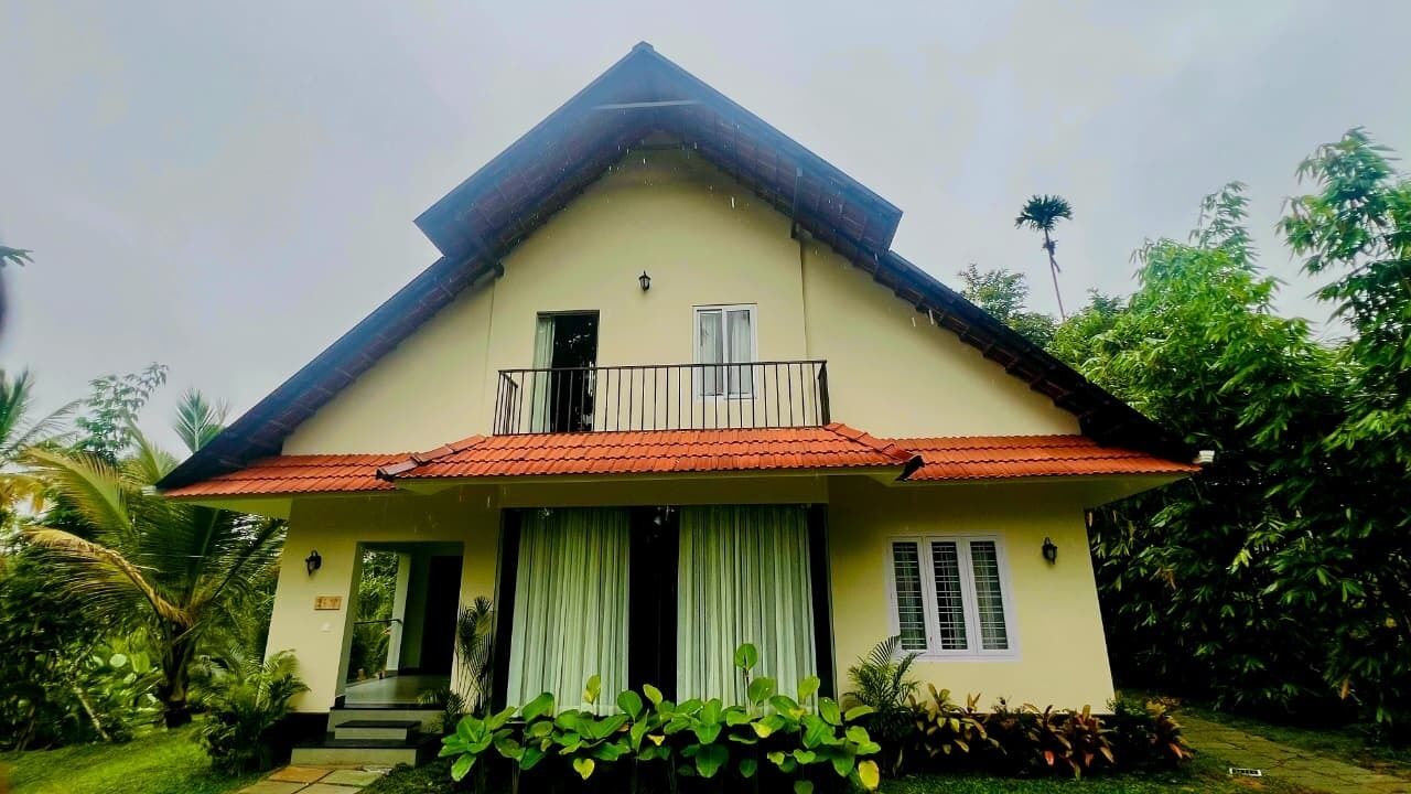 Een huis met twee verdiepingen, een rode pannendak, een balkon en een tuin met tropische planten.