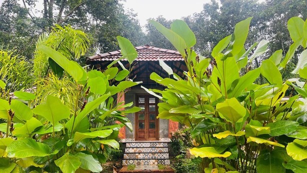 A traditional house with a tiled entrance and a red roof, surrounded by lush greenery.