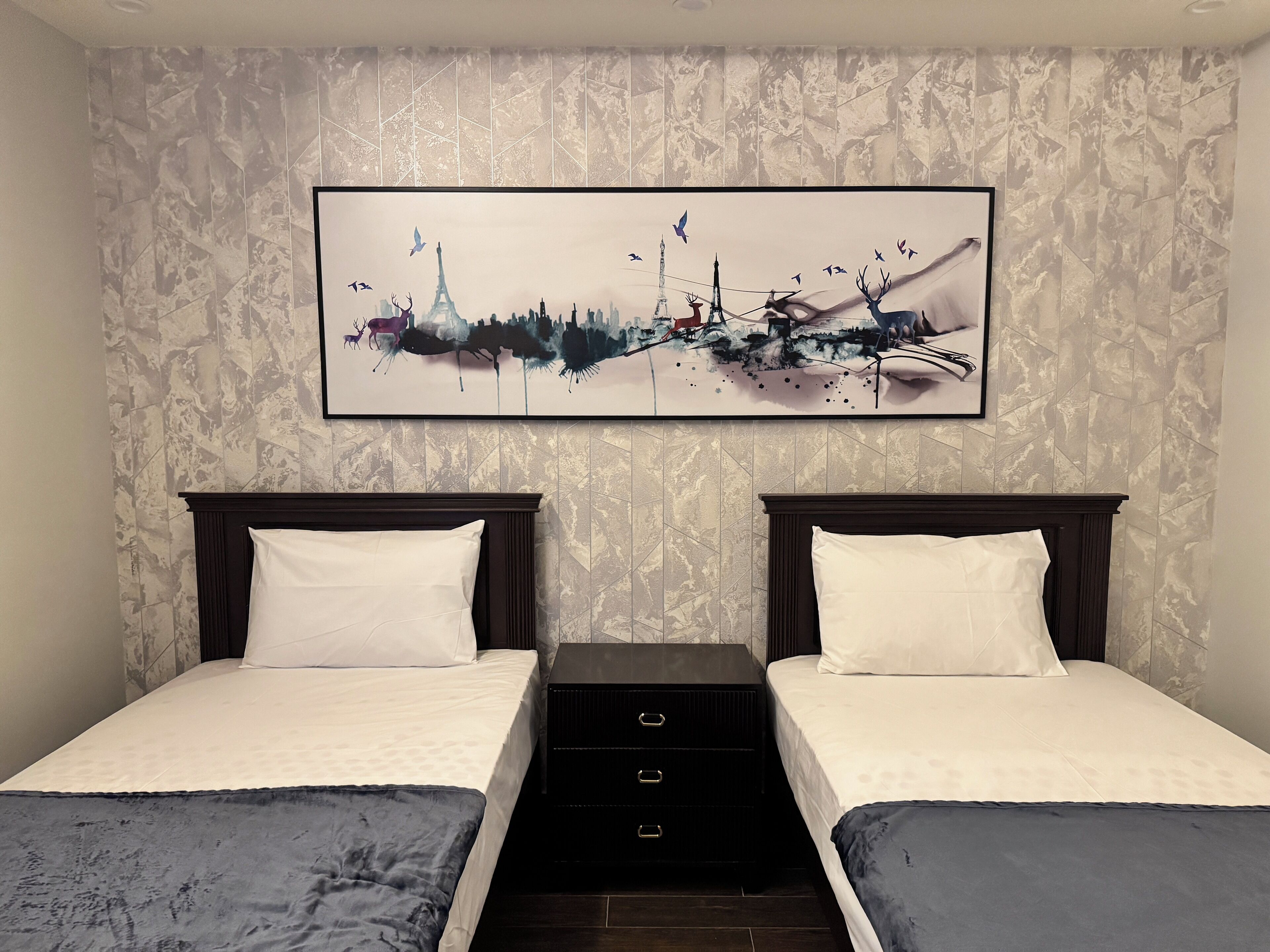 Une chambre d’hôtel avec deux lits, une grande peinture abstraite au mur et une commode de couleur sombre.
