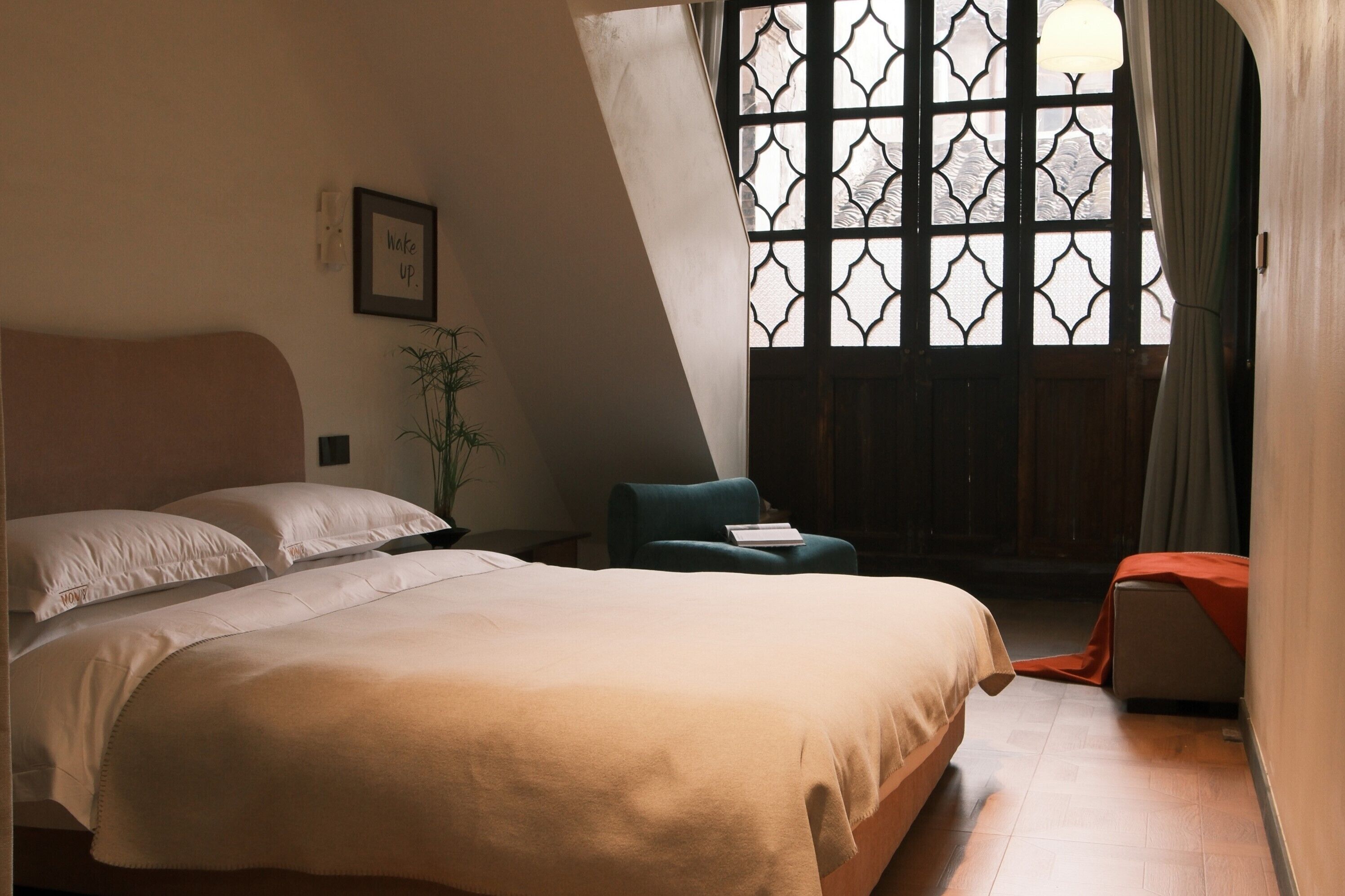 A bedroom with a large bed, a chair, a small table, and a window with a decorative grille.