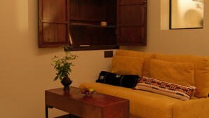 Una sala de estar con un sofá amarillo, una mesa de centro de madera, una planta en maceta y una estantería fijada a la pared.