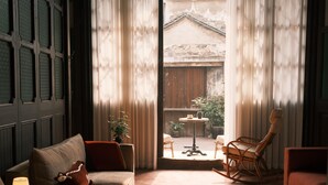 Una habitación acogedora con un sofá, un sillón mecedora, una pequeña mesa con una lámpara y vistas a un espacio exterior con una mesa y sillas de madera.